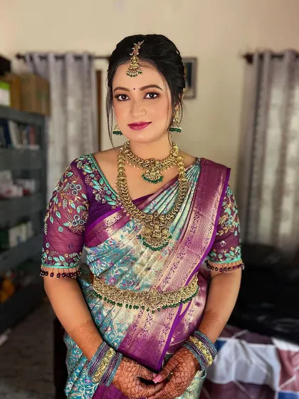 This bride from Mysore looks radiant in a unique peacock-toned silk saree. Her makeup features a soft pink and gold eye look with a matching lip color to complement her intricate floral blouse.
