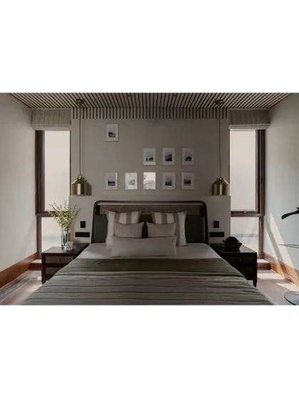 A bedroom in the Pràna project, where symmetry and calm reign. The slatted wood ceiling detail and matching pendant lights frame the bed, creating a cozy and contained sleeping nook.