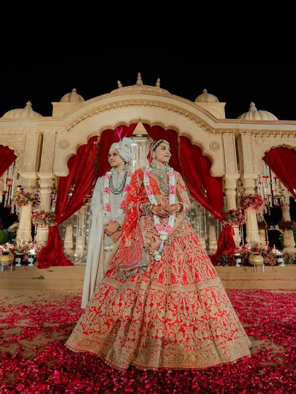 A picture of pure royalty and romance. The couple stands against a grand, traditional mandap, creating a timeless portrait of their wedding day.