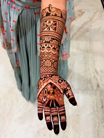 A close-up of the groom's portrait on the bride's hand. The artwork is framed by lotus motifs at the fingertips and intricate patterns on the arm.