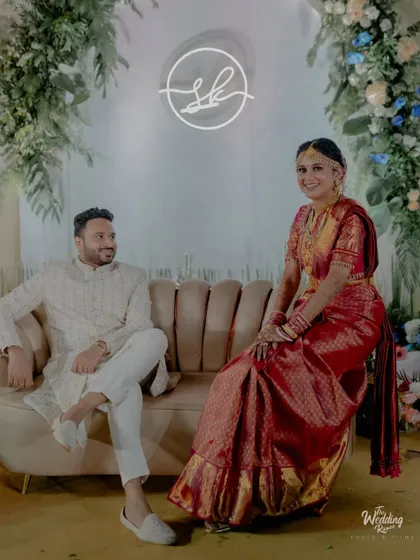 The couple poses on a stylish lounge sofa against a backdrop of white arches and greenery, a chic setup for post-ceremony photos.