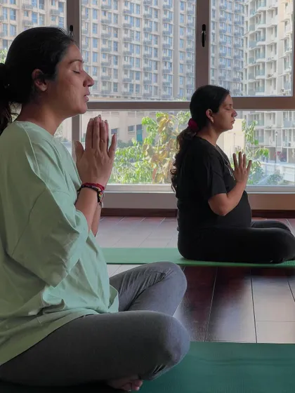 Two mothers-to-be sit in a moment of quiet meditation, hands in Anjali Mudra. Mental and emotional preparation is just as important as physical practice, and I guide you in finding your inner calm.