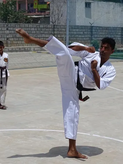 A senior student practices a side kick while a junior student observes. This is how skills are passed down in the dojo.