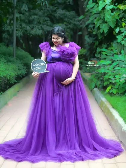 Announce your little one's arrival in style. An expecting mother in a purple tulle gown holds a 'Coming Soon' sign during her outdoor maternity session.