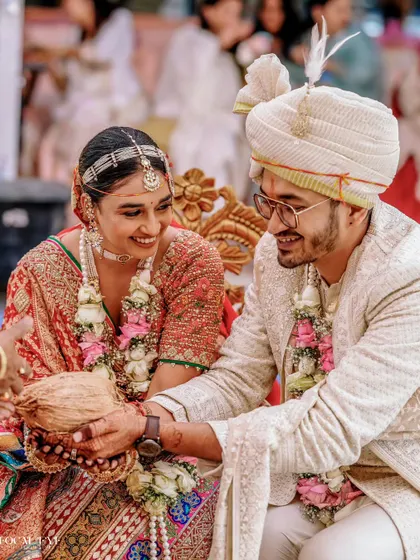 The couple participates in a wedding ritual with a coconut, their smiles showing the joy of the moment.