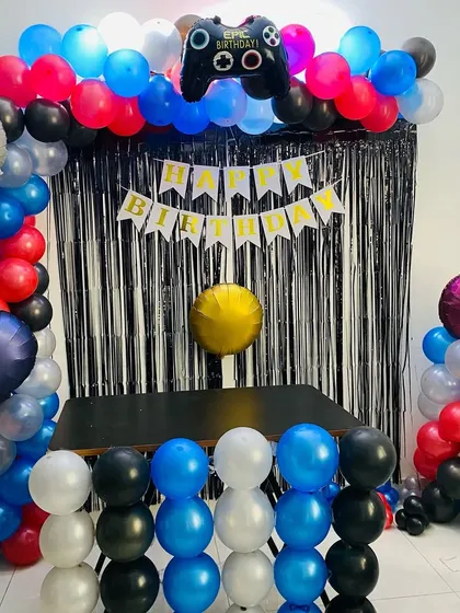 A gaming-themed birthday party with a balloon arch in blue, red, and black, and a controller-shaped foil balloon.