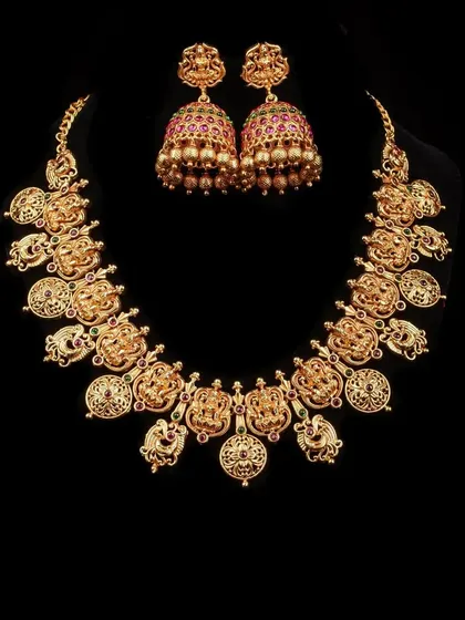 A classic temple jewellery set in an antique gold finish. The necklace features Goddess Lakshmi coin motifs, and it comes with perfectly matching jhumka earrings for a traditional look.