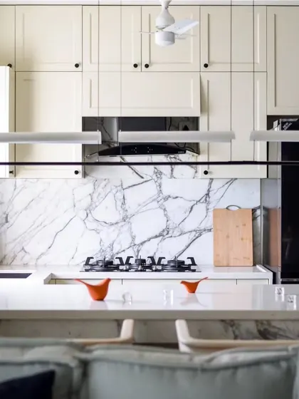 The kitchen is a culinary oasis with a classic European touch. White quartz countertops and a Statuario marble backsplash create a clean, pristine canvas, complemented by classic European-style cabinets.