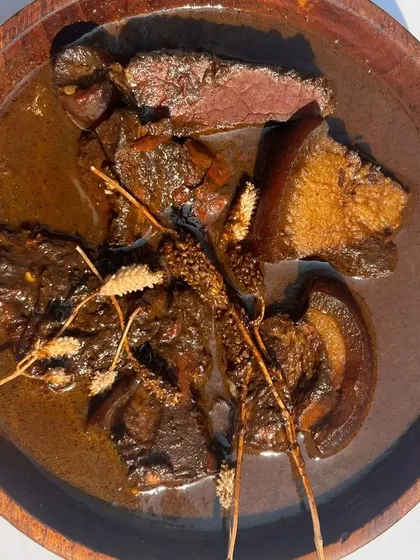 A bowl of our Smoked Pork with Anishi, garnished with wild herbs. This dish is a testament to the rich heritage of Naga cuisine, combining smoky meat with the deep, earthy flavors of the black curry.