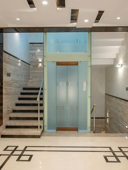 The lift and staircase area in the "Chic Adobe," showcasing travertine wall cladding and a geometric floor pattern.