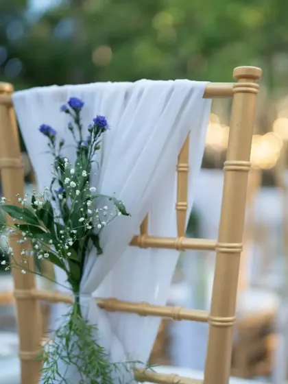 A simple yet elegant detail of a flower sprig tied to a chair with a sheer white ribbon for a classic wedding ceremony.