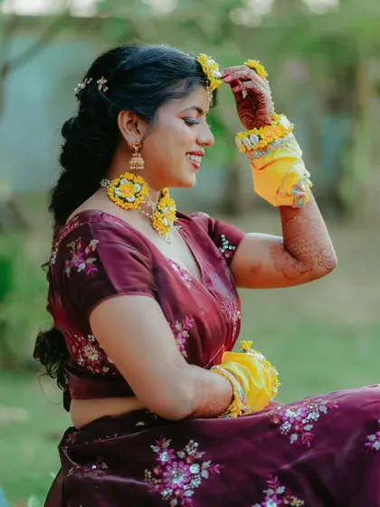 A candid side profile of the bride, smiling as she adjusts her floral maang tikka.