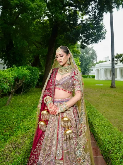A full-length view of this ethereal queen in her magnificent lehenga. The makeup is designed to be striking from a distance, with a radiant glow that stands out against the lush garden setting.