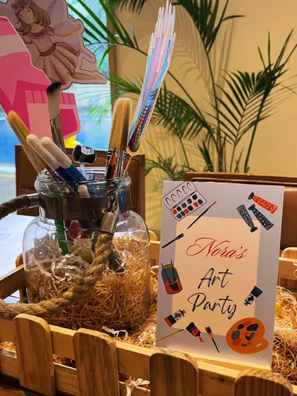 A themed centerpiece for the activity tables, featuring a jar of paintbrushes and a custom "Nora's Art Party" sign.