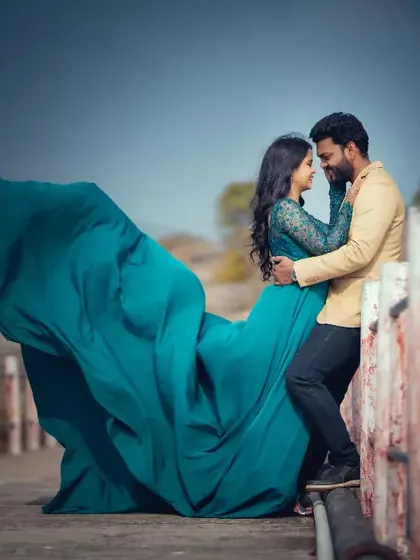 A dramatic pre-wedding photo with the bride's flowing teal gown against a rustic bridge, showcasing movement and color.