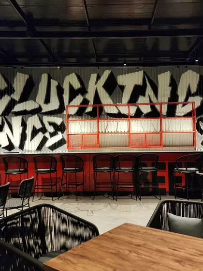 We used a bold, black-and-white graffiti style to paint "Clucking Stated 2018" on corrugated metal sheets behind the bar, giving the space an industrial, urban edge.