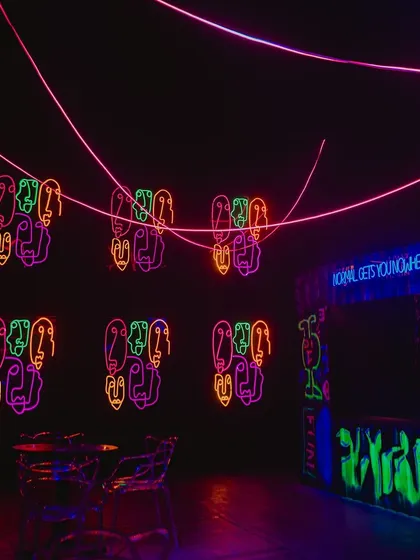 A view of the party space showing the neon signs and a graffiti art bar. We used UV paint and blacklights to make the artwork glow, adding to the underground club feel.