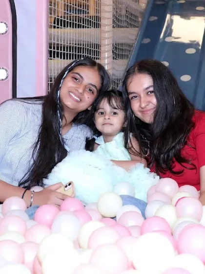 A birthday girl and her friends pose for a cute photo in the middle of the pink and white ball pit.