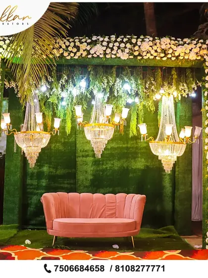 A beautiful and elegant photo booth or seating area. The green backdrop is adorned with white flowers and chandeliers, creating a sophisticated and intimate space.
