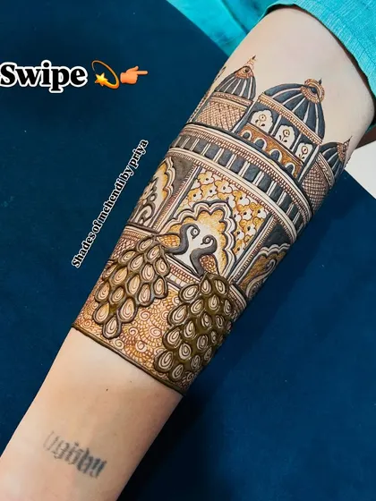 A swipe-to-see detail of the peacock and architectural elements on the arm. The shading and line work create a rich texture.