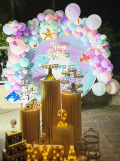 This under-the-sea themed party for a second birthday features a circular backdrop with whale and fish graphics. The pastel balloon arch is decorated with starfish and other sea creature cutouts for a complete aquatic feel.