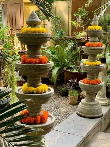 Two of our tiered granite temple lamps, decorated with marigold garlands, stand ready to illuminate a garden path for a celebration.