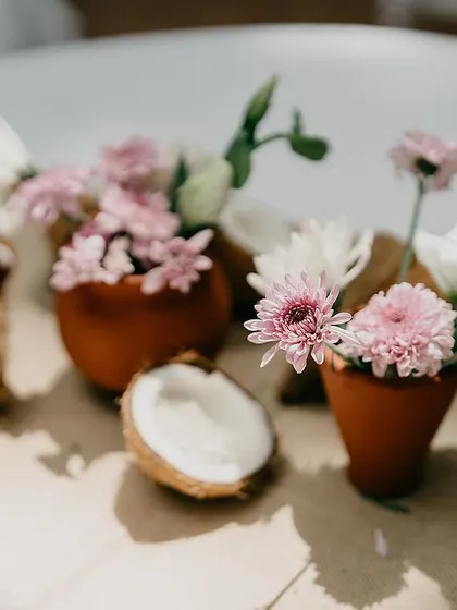 A delicate and beautiful centerpiece detail, with small flowers placed in coconuts and tiny terracotta pots for a touch of rustic charm.