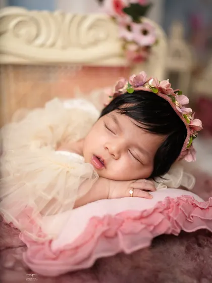 A close-up of a sleeping princess, showing her delicate features, a tiny ring, and a soft floral crown.