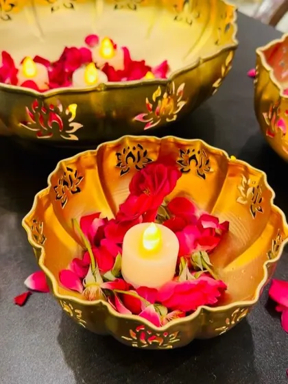 Our golden lotus-shaped urli bowls feature intricate cutwork that creates beautiful light patterns. They are shown here with rose petals and electric candles, demonstrating a safe and elegant decor option for office spaces.
