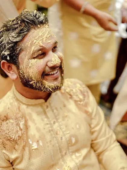 The groom smiling as he gets covered in turmeric paste by his friends and family.