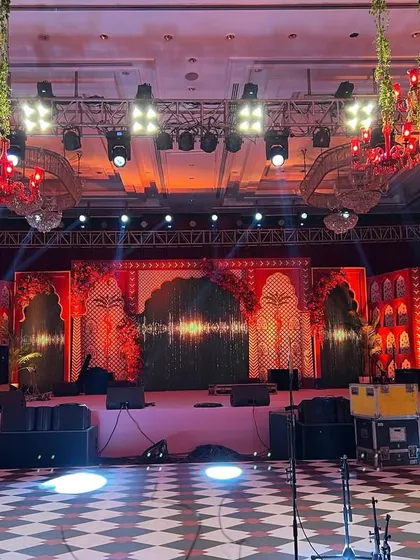 A wide shot of a stage with a traditional Rajasthani 'jharokha' design, a checkered dance floor, and red chandeliers hanging from the ceiling.
