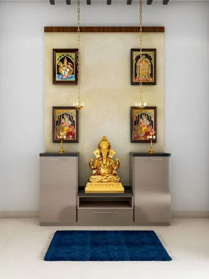This simple and elegant pooja setup features framed deities on the wall with hanging lamps. The symmetrical cabinets below provide storage and a platform for the main idol.