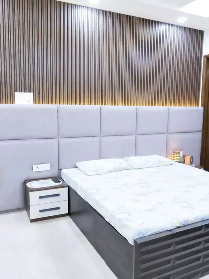 A bedroom featuring a tufted grey headboard against a backdrop of fluted wood paneling, creating a rich texture and a modern, sophisticated look.
