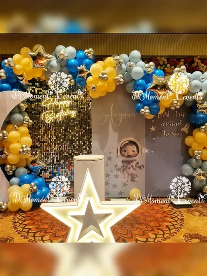 An out-of-this-world space-themed stage for a "First Trip Around the Sun," featuring a moon prop, a sequin wall, and a starry backdrop.