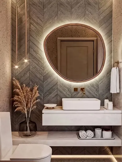 This bathroom design uses a mix of textures, including terrazzo-style walls and a chevron-tiled accent wall. The organically shaped backlit mirror serves as a beautiful focal point above the floating vanity.