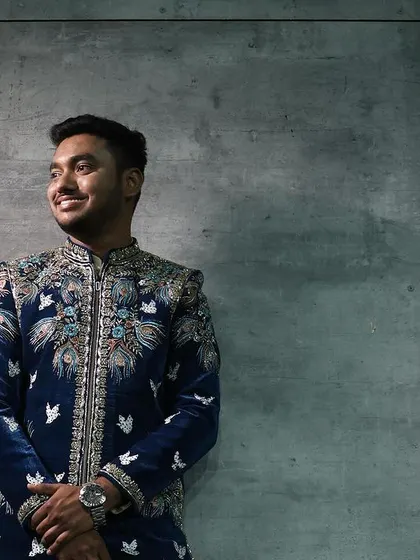 Another shot of the client in the royal blue velvet sherwani, showcasing the detailed bird-motif embroidery.