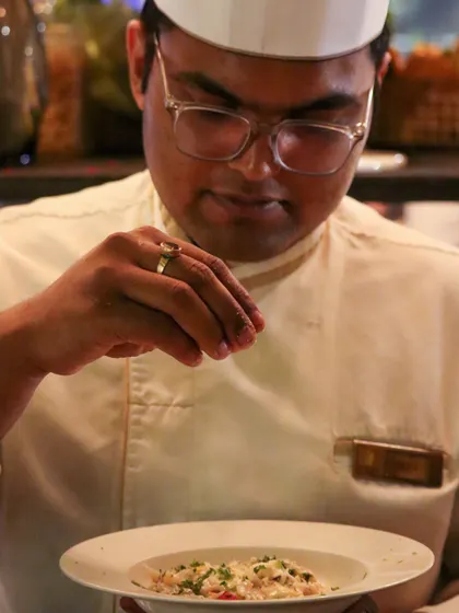 A chef adds the final seasoning to a dish with a practiced hand. This moment of precision captures the care and attention to detail that goes into every single plate we serve.