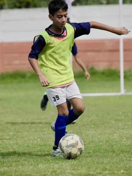 A young player in a yellow bib dribbling the ball with precision during a competitive match. This is the result of countless hours of ball mastery training.