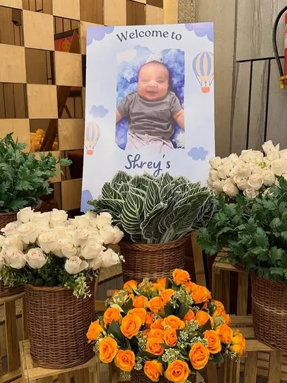 A personalized welcome sign for baby Shrey's party, surrounded by beautiful fresh flower arrangements in baskets.