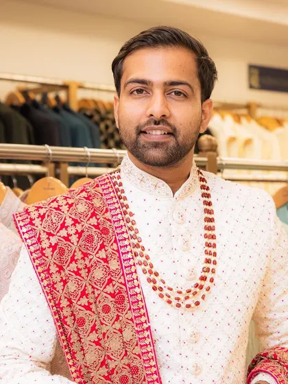 Another happy client ready for a wedding, wearing our white sherwani complemented by a vibrant red and gold stole and a beaded necklace.