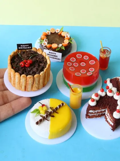 A hand holding a collection of miniature cakes, showing their small scale and intricate details.