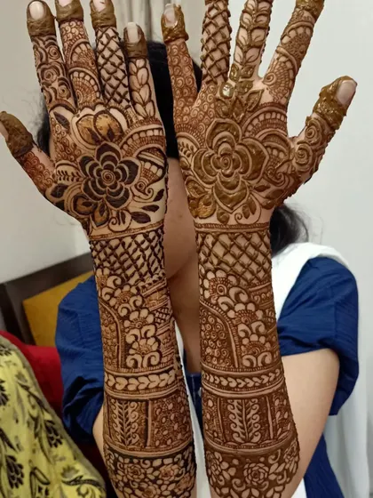 A full view of a happy client showing her completed bridal henna. The design features large floral motifs on the palms and intricate bands of patterns all the way up the arms.