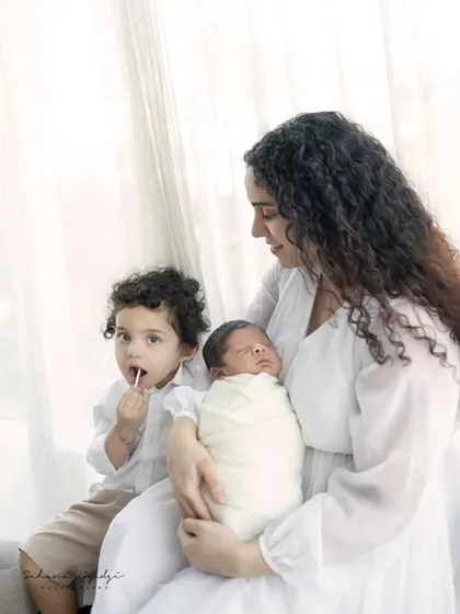 A candid moment during a newborn session, where the older brother is enjoying a lollipop while his mother holds the new baby. It shows the real, unscripted life of a growing family.
