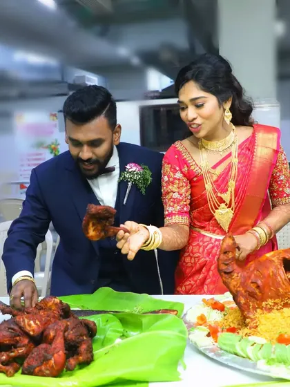 A happy couple admiring the grand feast prepared for them, including a whole roasted chicken and a platter of fried chicken pieces.