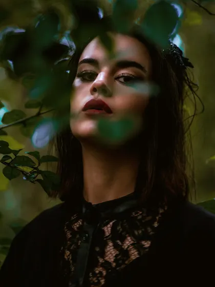 A close-up portrait from the jungle editorial. Peeking through the leaves adds a sense of mystery and intimacy, drawing the viewer into the frame.