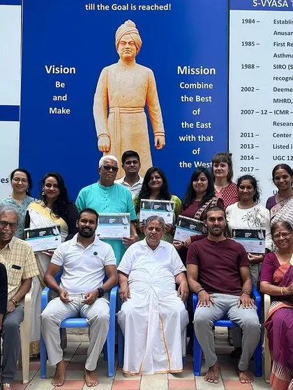 A group photo with students and faculty at the S-VYASA campus. The university's vision and mission, displayed behind us, guide our work in combining the best of the East and West.