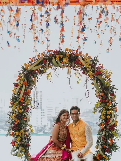 The couple shares a dance on a floral swing at their rooftop Mehndi, with the city skyline providing a stunning modern backdrop.