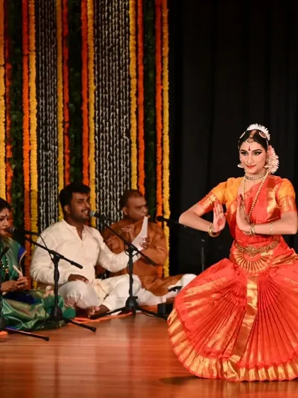 Kavya Navani in a moment of devotion during her arangetram, with the live orchestra providing the soulful musical foundation. This image captures the synergy between the dancer, the musicians, and the art form.