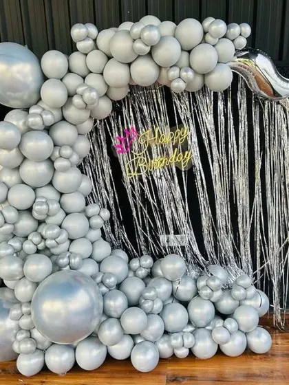 A modern birthday backdrop with a silver shimmer curtain and a full arch of silver balloons.