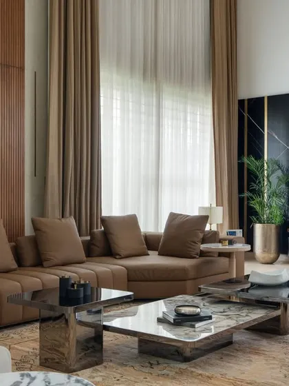 The double-height living area in the Celadon project features a striking black marble wall with brass inlays for the media unit, contrasting with the warm wood paneling. The large sectional sofa and layered coffee tables create a comfortable yet sophisticated space for family gatherings.